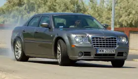 Szary Chrysler 300S z dymiącymi oponami, kierowca za kierownicą, na drodze.