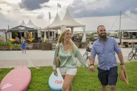 Glückliches Paar spaziert am **Stein Ostsee Strand** entlang, vorbei an SUP-Boards und Strandbuden.