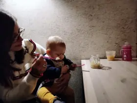 Mamma dà la pappa al suo bimbo fuori casa, con un vasetto di omogeneizzato e un biberon pronti.