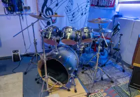 Der **Aufbau Schlagzeug** ist bereit für den nächsten Gig. Glänzende Trommeln und Becken stehen auf stabilen Stativen, beleuchtet von blauem Licht.