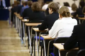 Uczniowie siedzą w rzędach przy ławkach, skupieni na rozwiązywaniu pytań maturalnych.