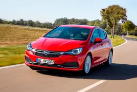 Czerwony Opel Astra jedzie po krętej drodze. W tle pola i drzewa. Idealny do diagnostyki z **op-com opel po polsku**.
