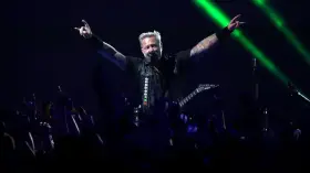 James Hetfield, un des membres de Metallica, salue la foule avec les cornes du diable, éclairé par des faisceaux verts.