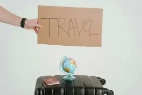 Ręka trzyma tabliczkę z napisem TRAVEL. Obok walizka, globus i paszport. Czy to zapowiedź kolejnych pozytywnych emka travel opinie?