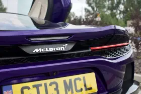 Fioletowy McLaren GT z otwartymi drzwiami, widok na tył z logo i tablicą rejestracyjną.