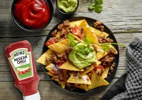 Nachos con carne, guacamole y salsa en un plato negro, con botella de Heinz y cuencos de salsa.