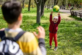Un enfant joyeux lance un ballon en l'air dans un parc, un autre enfant est devant.