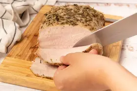 Un jugoso lomo a la sal, cubierto de hierbas, se corta en rodajas tiernas sobre una tabla de madera.