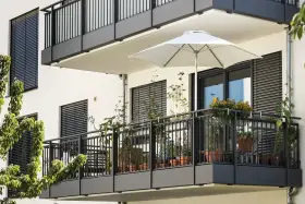 Nowoczesny balkon po remoncie, z białym parasolem i doniczkami pełnymi zieleni.