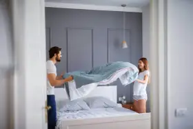 Coppia felice che cambia le lenzuola, un gesto che ci ricorda ogni quanto cambiare le lenzuola per un sonno più sano.
