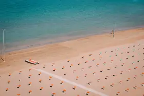 Pusta plaża w Rimini z rzędem pomarańczowych parasoli i turkusową wodą. Na piasku stoi mała łódź.