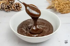 Cuchara con ganache de chocolate cayendo en un cuenco blanco. El chocolate es brillante y sedoso, perfecto para postres.