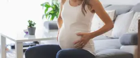 Kobieta w ciąży siedzi na kanapie, dotykając brzucha. Zauważyła brązowe plamienie w ciąży, co ją martwi.