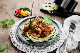 Spaghetti z cukinii z kurczakiem i warzywami w sosie na talerzu.