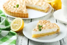 Un delicioso pastel de limón con merengue dorado, acompañado de limones frescos y una servilleta a cuadros verdes. Los ingredientes del lemon pie lucen perfectos.
