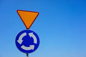 Znak ustąp pierwszeństwa i znak informujący o ruchu okrężnym na tle błękitnego nieba.