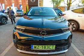 Czarny Opel z zieloną tablicą rejestracyjną WZ 183CT na tle innych samochodów.