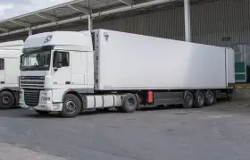 Biała naczepa DAF XF z chłodnią, gotowa do transportu. Obok stoi kolejna ciężarówka, tworząc zgrany zespół pojazdów.