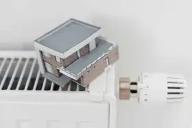 Model domu na grzejniku symbolizuje wysokie koszty ogrzewania i potrzebę dopłat do prądu.