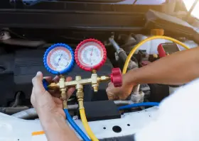 A mechanic uses a manifold gauge set to check for a freon leak in a car's AC system.