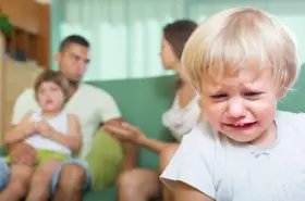 Płacz dziecka na pierwszym planie, rodzice z drugim dzieckiem na kanapie w tle. Czy to zimny chów dzieci?