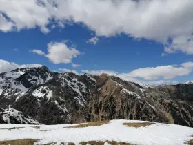 Cimon di Bolentina, un maestoso panorama montuoso con cime innevate e un cielo azzurro punteggiato di nuvole bianche.