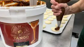 Un repostero decora galletas con una manga pastelera, usando el delicioso dulce de leche de un gran envase.
