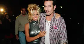Pamela Anderson i Tommy Lee, ikony lat 90., pozują do zdjęć. Pamela w błyszczącej sukience, Tommy w kratowanej koszuli.