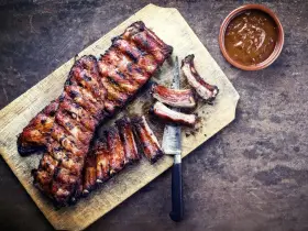 Soczyste żeberka w miodzie, grillowane do perfekcji, podane na desce z sosem.