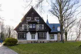 Pałac myśliwski w Promnicach, z charakterystyczną architekturą szachulcową i zdobieniami, otoczony drzewami.