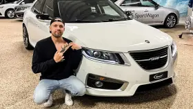 Man med hjort-tatuering på bröstet poserar framför en vit Saab.