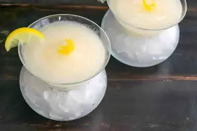 Dos copas de sorbete de limón, una con rodaja de limón y rizo de piel, servidas sobre hielo picado.