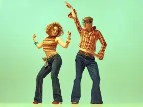 Para tańczy w rytm disco, ubrana w stylowe dzwony i wzorzyste topy, uosabiając modę lat 70.