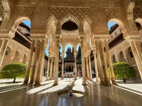 Intricate arches and columns of the Alhambra, a perfect postcard from Granada. Sunlight streams through, illuminating the detailed stonework.