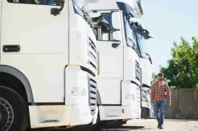 Kierowca idzie obok rzędu białych ciężarówek. To właśnie spedycja co to – transport towarów na dużą skalę.