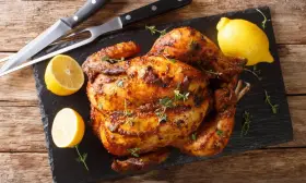 Pollo al horno dorado y jugoso, adornado con tomillo fresco y acompañado de limones cortados. Un festín listo para servir.