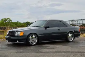 Ciemnoszary Mercedes "Hammer" coupe z przyciemnianymi szybami i chromowanymi felgami stoi na mokrej drodze.