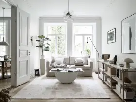 Salón con sofá beige, mesa de centro de cristal y alfombra clara. Decoración minimalista y plantas, creando un ambiente de feng shui.