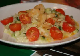Risotto z krewetkami i pomidorkami koktajlowymi na białym talerzu.