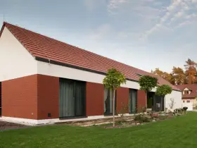 Wizualizacja: nowoczesny dom z białymi ścianami, ceglaną elewacją i czerwonym dachem.