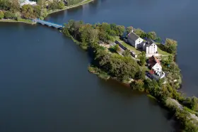 Ełk: zamek krzyżacki na wyspie, idealne miejsce na zwiedzanie. Most prowadzi do historycznych budynków otoczonych zielenią i wodą.