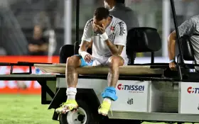 Neymar siedzi na wózku golfowym, zakrywając twarz dłońmi. Jego kontuzja jest widoczna, a zawodnik wygląda na zrozpaczonego.