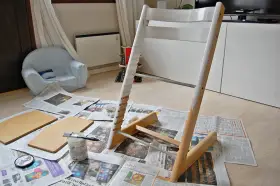 Måla om Stokke stol med vit färg. Trädelar och pensel ligger på tidningspapper.