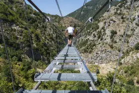 Un ponte tibetano in Puglia attraversa una gola verdeggiante, con persone che camminano su passerelle metalliche sospese tra montagne.