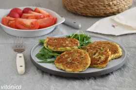 Tortitas de calabacín doradas y esponjosas, servidas sobre rúcula fresca. Acompañadas de una ensalada de tomate y rábano.