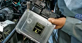 Mechanik trzyma komputer sterujący silnikiem do mapowania. Widoczny symbol VW.