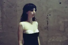 Stella Rose Gahan w czarnej sukience z białym gorsetem, stoi przy betonowej ścianie.