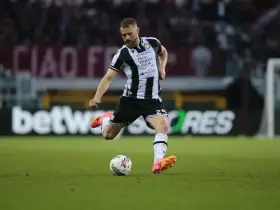 Piłkarz Jesper Karlström w czarno-białej koszulce Udinese Calcio kopie piłkę na zielonej murawie stadionu.