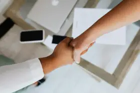Uścisk dłoni symbolizujący podpisanie umowy na czas nieokreślony. Na stole leży laptop i dokumenty.