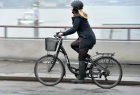 Kvinna cyklar på en elcykel, kanske med bidrag för att underlätta pendlingen. Hon bär hjälm och en varm jacka.